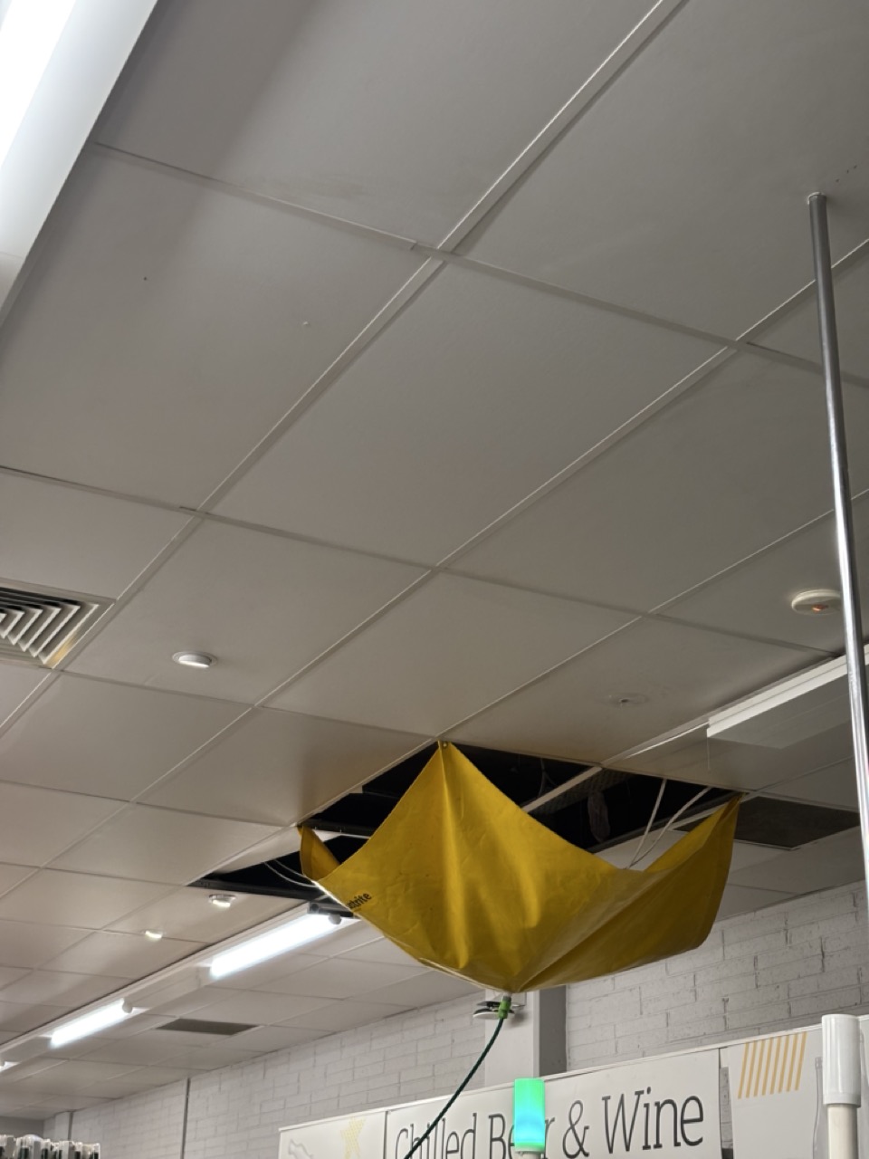 Photograph of supermarket interior, ceiling panels replaced with a leak protection device that resembles an inverted umbrella